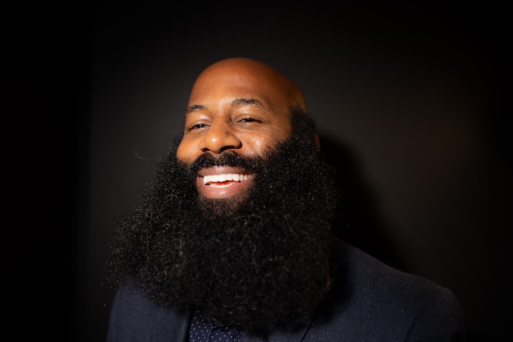 Original studio portrait of Anson laughing warmly in a dark tailored jacket and polka-dot collared shirt, preserving his full beard and natural expression.